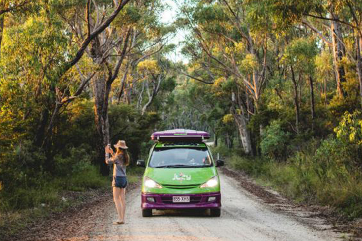 girl stops to take photo in front of jucy van raod tripping in australia