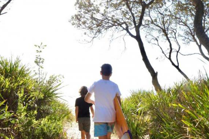 2 people walking to a beach with a surfboard